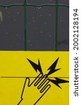 A piece of fence with a yellow warning sig n: Warning, electric fence . German attention sign " Vorsicht Elektrozaun " . Be aware of electricity damage symbol with blizzards and hand on wire .