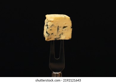 A Piece Of French Blue Cheese On A Fork On A Black Background. Close-up