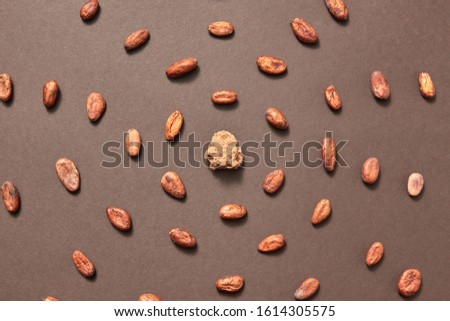 Piece of fresh natural cocoa mass in the middle of food pattern from cacao beans on a brown background, copy space. Top view. Dry ingredients for making dark chocolate.