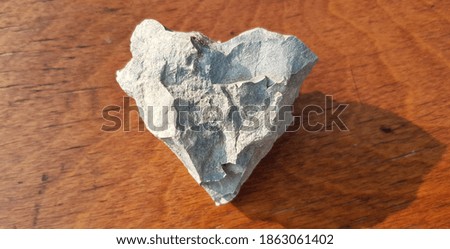A piece of gray hardened cement in the shape of a heart, on a brown wooden table (top view).