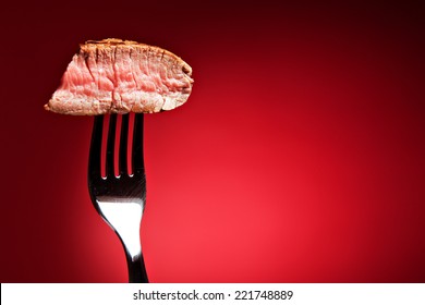 Piece Of A Grilled Steak On A Fork Isolated On Red