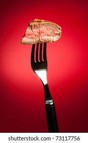 Piece Of A Grilled Steak On A Fork Isolated On Red