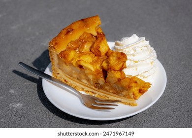 A piece of homemade apple pie in white plate served with whipping cream on the side, A pie in which the principal filling ingredient is apples, The earliest printed recipe is from England. - Powered by Shutterstock