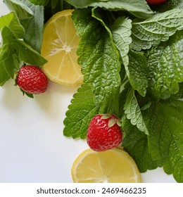 A piece of lemon with lemon balm and strawberries. On a white plate are large lemon balm and mint leaves, lemon wedges and two strawberries - Powered by Shutterstock