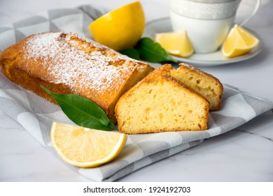 Piece of lemon cake on kitchen towel with lemons and tea cup. Easy recipe of citrus dessert for everyday cooking. Homemade bakery by classic recipe.Traditional English tea time treat.