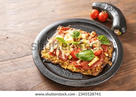 Piece of low carb pizza on a crust from zucchini and oat flakes, topped with tomato, feta cheese, salami and basil, dark plate on a wooden table, copy space, selected focus, narrow depth of field