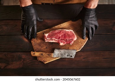 A piece of meat on the board near the butcher's knife. Butcher in black gloves.