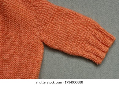 Piece Of Orange Small Wool Knitted Sweater With One Sleeve On Gray Table