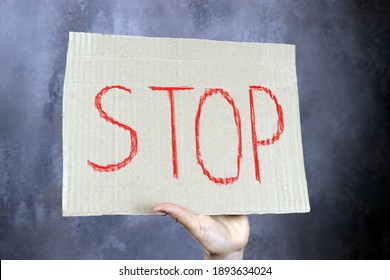 Blatt Papier mit dem Wort "Stopp in der Hand"auf grauem Hintergrund