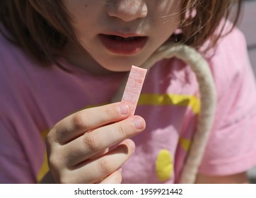 A Piece Of Pink Chewing Gum In The Girl's Hands. In The Background She Opened Her Mouth.