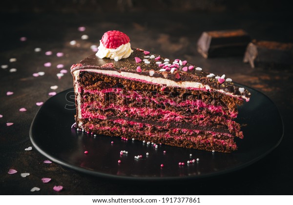 Piece of raspberry chocolate torte on a black\
plate on dark brown\
background