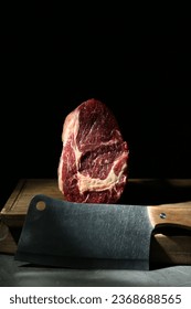 Piece of raw beef meat and knife on grey table against black background - Shutterstock ID 2368688565