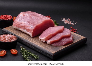 A piece of raw fresh pork on a wooden cutting board with spices and herbs on a dark concrete background - Powered by Shutterstock