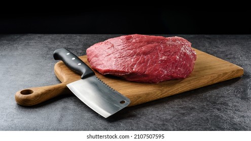 A piece of raw meat and a knife lie on a cutting board on a dark background with copy space. - Powered by Shutterstock