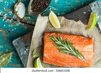 A piece of raw salmon, spices, knife, board, spoon, olive oil, lemon on the old shabby blue table close-up view from above. Preparation for cooking fish food. Salmon steak.