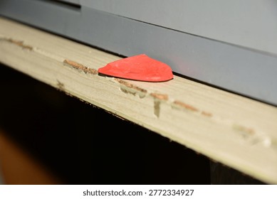 A piece of red triangular tailor's chalk resting on the edge of a worn wooden workbench next to a grey sewing machine