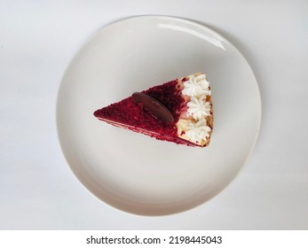 A Piece Of Red Velvet Looks Up In The Shape Of A Triangle. With A Sprinkle Of Red Powder And Whipped Cream.