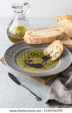 A piece of rustic bread dipped into balsamic vinegar and olive oil with a bottle of olive oil in behind.