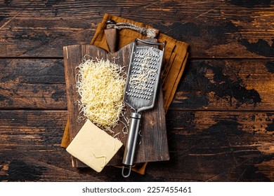 Piece of semi hard cheese and grated cheese with grater. Wooden background. Top view.