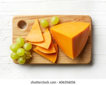 Piece And Slices Of Cheddar Cheese On Cutting Board. From Top View