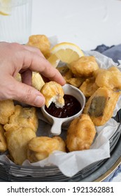 A Piece Of Tempura Hake Held By A Man Hand About To Be Spread With Barbecue Sauce.