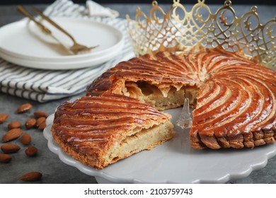 A piece of traditional French galette des rois with golden crown, almonds plate and cutlery. Cake made with puff pastry and creamy paste filling roll in circle shape. It's usually served on Epiphany - Shutterstock ID 2103759743