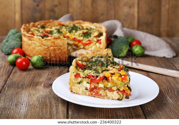 Piece of Vegetable pie with\
broccoli, peas, tomatoes and cheese on plate, on wooden\
background