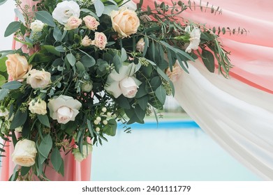 A piece of wedding arch adorned with flowers and cloth. Flower arrangement consists of different types of roses and greenery