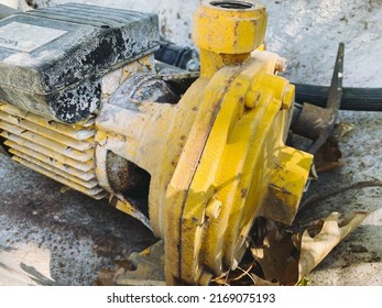 A Piece Of Yellow Metal Reinforcement Lies On The Ground. Old, Yellow Battery With Clutch. Broken Truck Part.