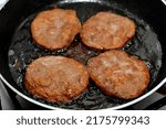 pieces of beef burger being fried on shallow oil on a frying pan, meat burgers cutlet shaped patty made of minced meat and it