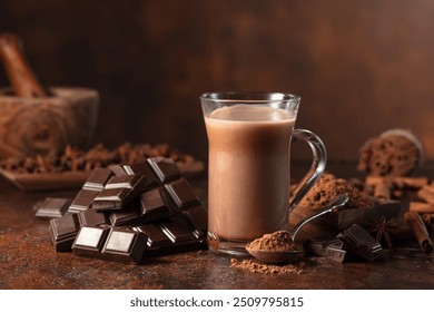 Pieces of bitter chocolate and glass of cocoa drink on a brown vintage table. Copy space.