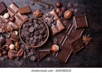 Pieces Of Broken Tasty Milk And Dark Chocolate Bars With Drops, Cocoa Beans And Hazelnut On Black Meta Background