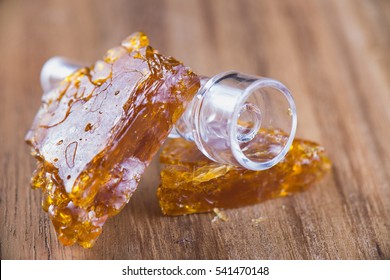 Pieces of cannabis oil concentrate aka shatter with glass rig bowl over wood background