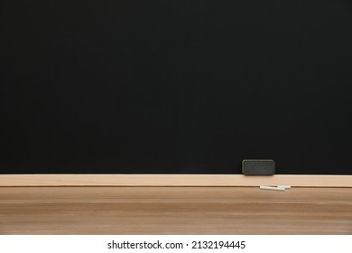 Pieces of chalk and duster on wooden table near blackboard, space for text