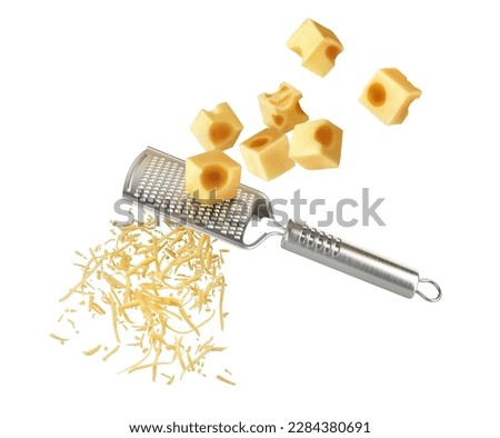 Pieces of cheese falling on a grater with cheese shavings on a white background