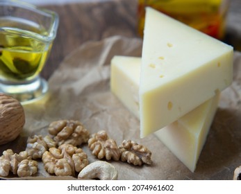 Pieces Of Cheese On Parchment Paper With Nuts And Olive Oil On An Old Wooden Table