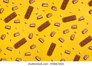 Pieces chocolate bar on a background of peanuts. Modern composition on yellow  background 