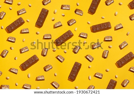 Pieces chocolate bar on a background of peanuts. Modern composition on yellow  background 