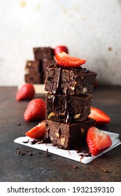 Pieces of chocolate brownie with strawberries on brown background