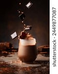 Pieces of dark chocolate fall into a glass of cocoa drink creating a beautiful splash.