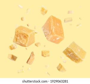 Pieces of delicious parmesan cheese flying on yellow background