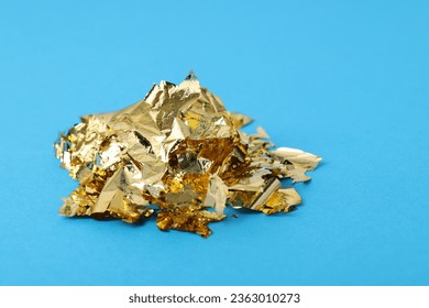 Pieces of edible gold leaf on light blue background, closeup
