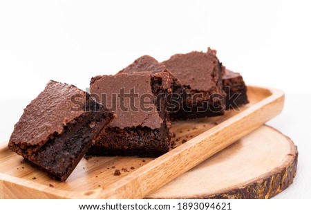Pieces of fresh chocolate brownie on wooden plate on white background. Stack of fudgy chocolate brownies on white background, homemade bakery and dessert. Brownie chewy squares stack on wooden plate.