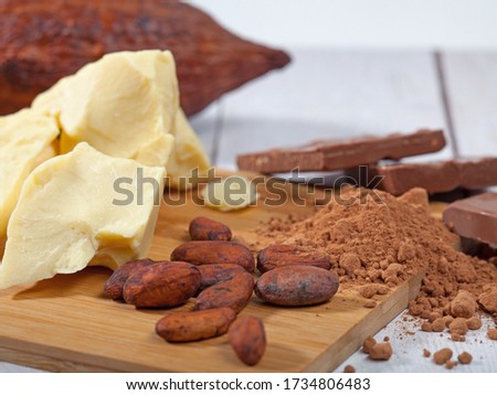 Pieces of natural cocoa butter, bar of milk chocolate, cocoa powder, cocoa pod and cocoa beans on wooden cutting board