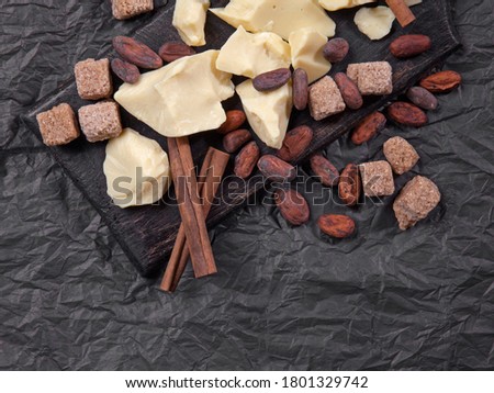 Pieces of natural cocoa butter with cinnamon, cocoa beans and cane sugar on black background. Top view with copy space