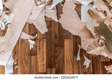 Pieces Of Old Torn Wallpaper Lie On The Wooden Floor. Background With Copy Space. Room Renovation Concept