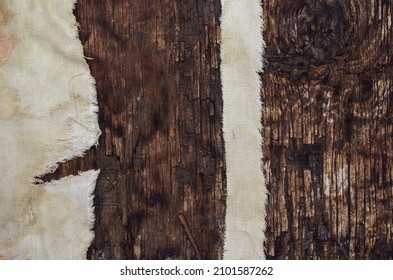 Pieces Of Old Worn Cloth On Textured Wood Surface. Wide And Narrow Ribbon With Uneven Jagged Edge On Dark Burnt Wood. Top View. Selective Focus.