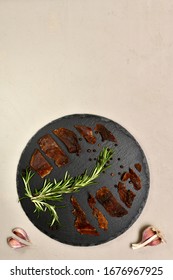 Pieces Of Rabbit Meat Are Laid Out On A Round Black With Rosemary Garlic Pepper On A Plaster Vertically At The Bottom.