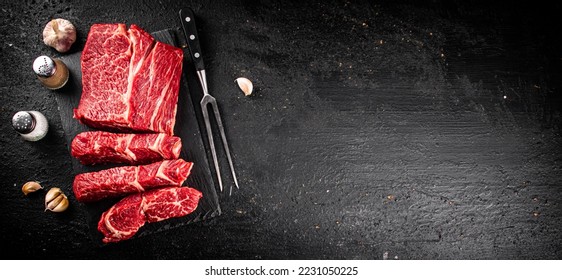 Pieces of raw beef on a stone board. On a black background. High quality photo - Shutterstock ID 2231050225