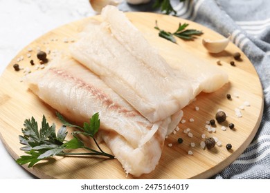 Pieces of raw cod fish, spices and parsley on table, closeup
